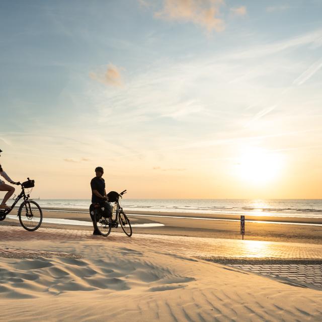 Cyclistes regardant le coucher de soleil sur la plage de Leffrinckoucke